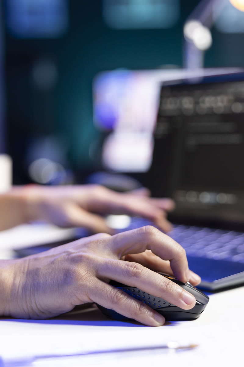 Un développeur web au travail : la main droite sur la souris, la gauche sur le clavier d’un ordinateur portable où s’affiche du code.
